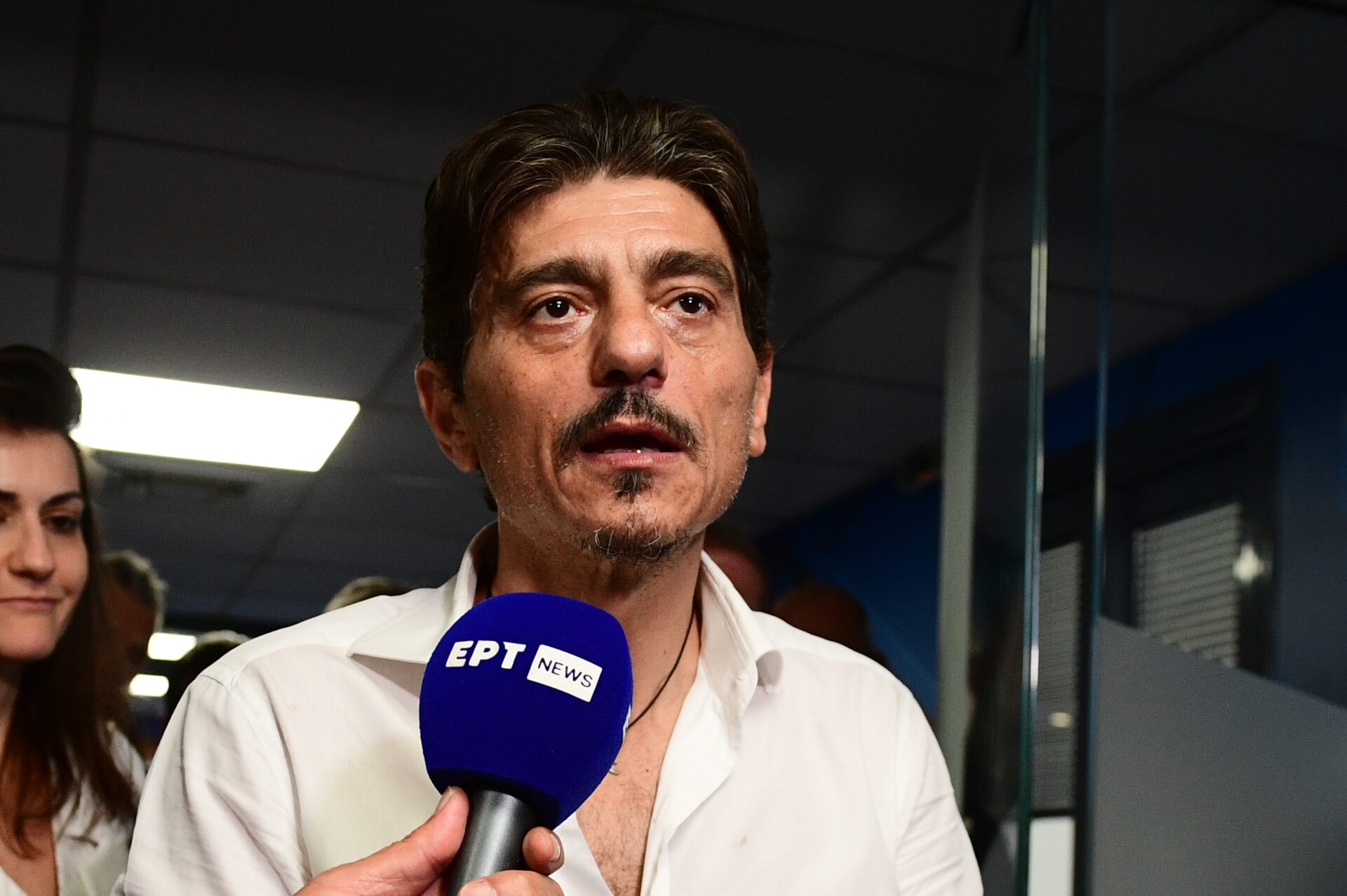 Dimitris Giannakopoulos speaking into a microphone in an interior
